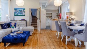 Een woonkamer met een bank, een voetenbankje en een eethoek met stoelen en een tafel.