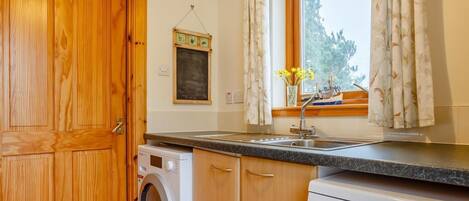 Cocina compacta con armarios de madera, lavadora, lavavajillas y una ventana con cortinas.