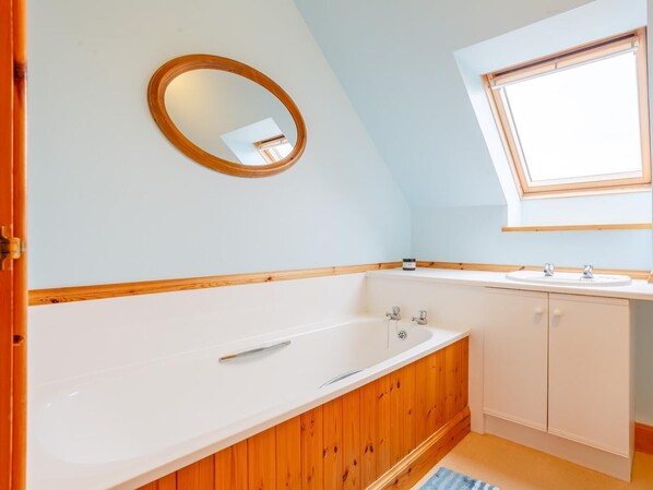 A bathroom with a wooden vanity, a freestanding bathtub, and a skylight.