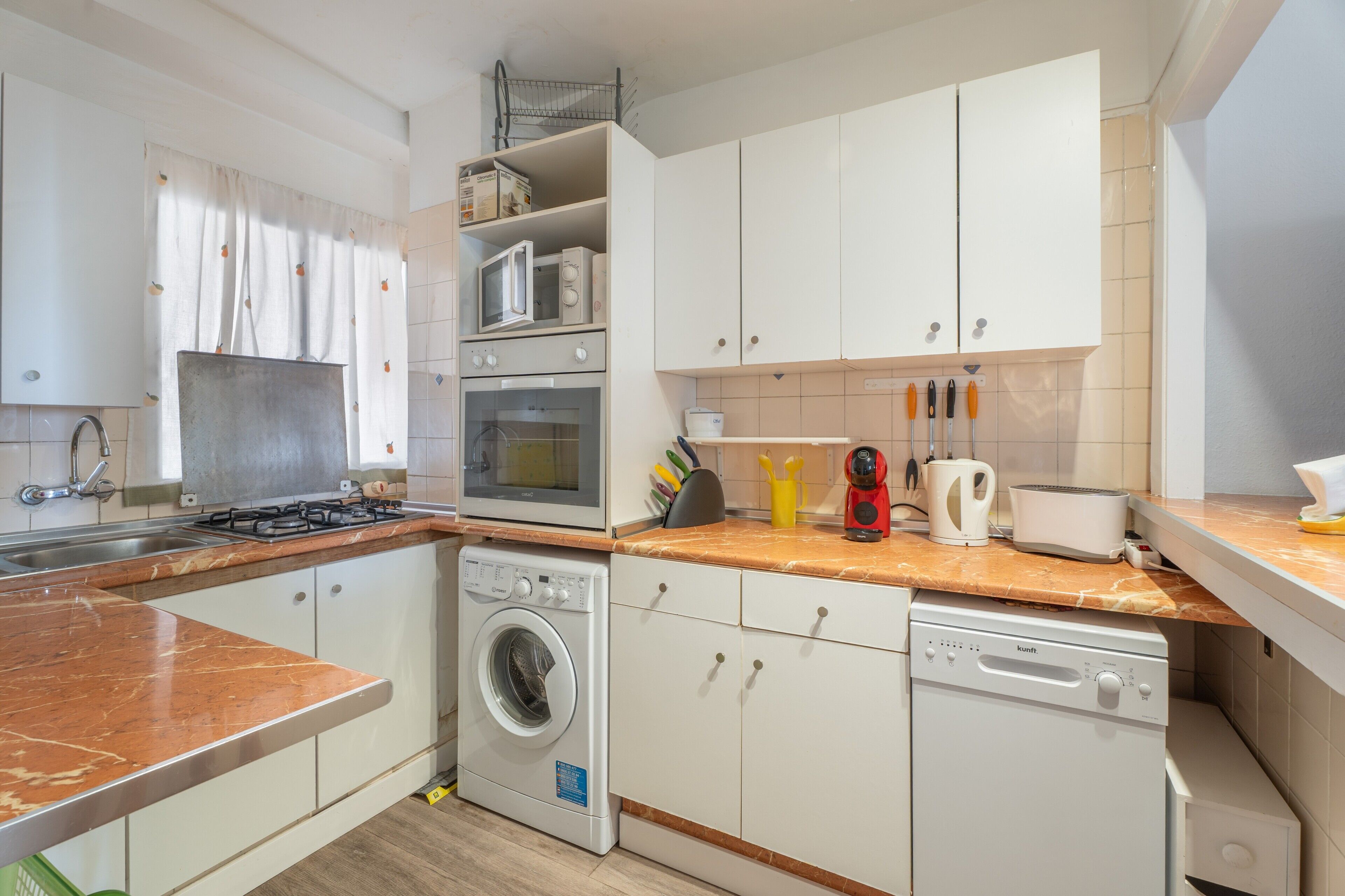 Een kleine keuken met een gasfornuis, oven, magnetron en een ingebouwde wasmachine.
