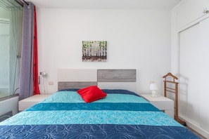A bedroom with a bed, a nightstand, a lamp, a wall art piece, and a window with curtains. - Fantastic 1-Bedroom Apartment with Sea Views, Pool, and Air Conditioning (Costa Adeje)