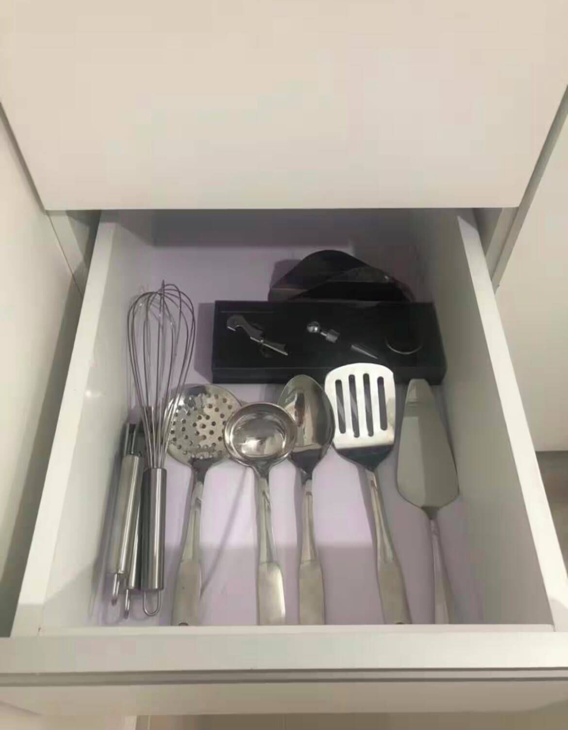 Un tiroir contenant des ustensiles de cuisine, notamment un fouet, une spatule et une louche.