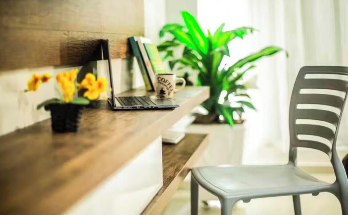 Uma mesa de madeira com um laptop, uma caneca e um vaso de planta.
