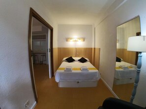 Una camera d'albergo con un letto, una lampada da comodino, uno specchio e un piccolo tavolo con una sedia.