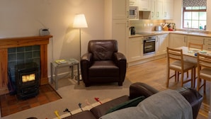 Ein Wohnzimmer mit Kamin, einer Ledersofa, einem Essbereich mit Holzsesseln und einer Küche mit weißen Schränken.