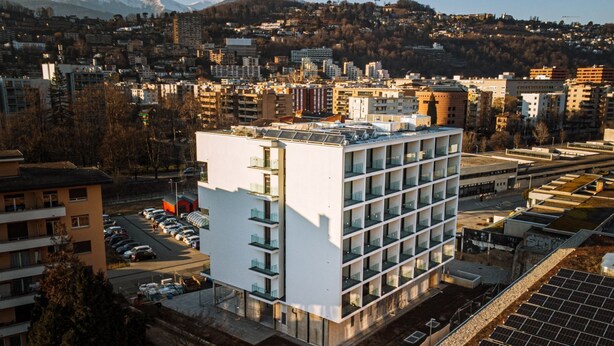 Un bâtiment moderne à plusieurs étages, doté d’un parking et de panneaux solaires.