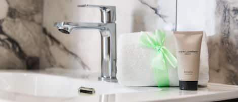 Un lavabo de salle de bain avec un mur en marbre, une serviette et un flacon d’après-shampoing Balsamo.