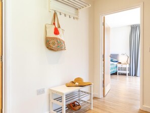 Ein Flur mit Kleiderständer, einem kleinen Tisch mit Hut und einem Blick in ein Schlafzimmer mit Bett und Vorhängen.