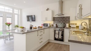 A modern kitchen with white cabinetry, a built-in oven, a microwave, and a large window. - 1 Bed in Colwyn Bay (oc-78154) (Hen Golwyn)