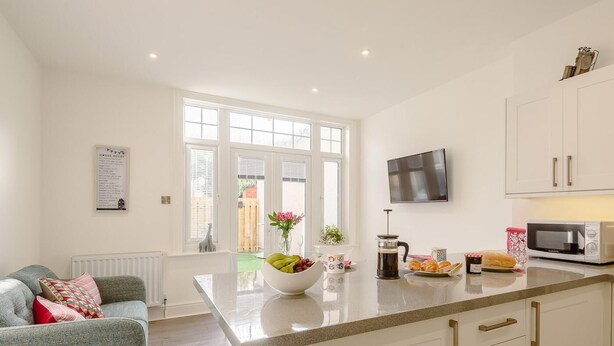 A modern kitchen with white cabinetry, a large window, a flat-screen TV, and a coffee maker on the counter. - 1 Bed in Colwyn Bay (oc-78154) (Hen Golwyn)