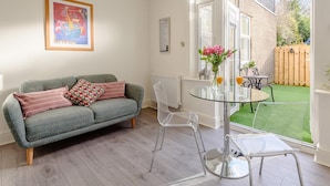 A living room with a grey sofa, clear chairs, a glass table, and a painting on the wall. - 1 Bed in Colwyn Bay (oc-78154) (Hen Golwyn)