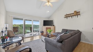 Ein Wohnzimmer mit Sofa, Couchtisch und Fernseher, ein Balkon mit Aussicht und einem Deckenventilator.