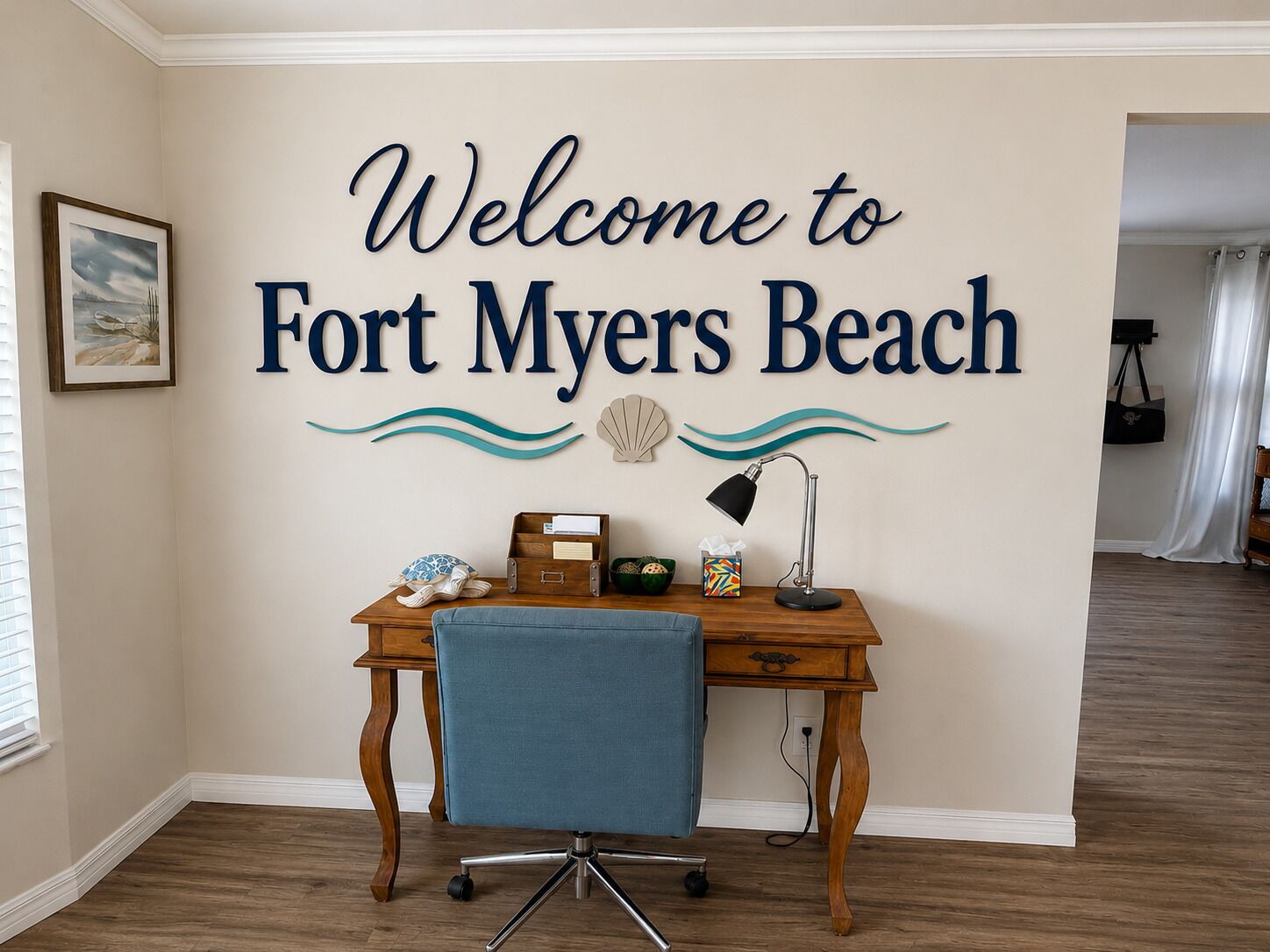 Une pièce comprenant un bureau, une chaise, un tableau encadré et une pancarte murale sur laquelle on peut lire : « Bienvenue à Fort Myers Beach. »