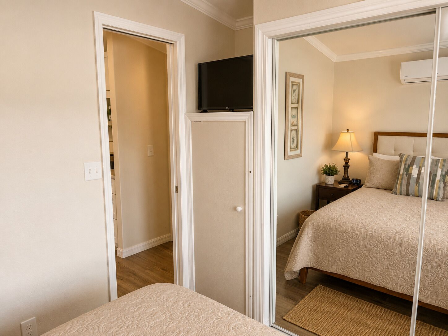 Une chambre à coucher avec un lit, une table de chevet avec une lampe, un téléviseur fixé au mur et une porte donnant sur une autre pièce.