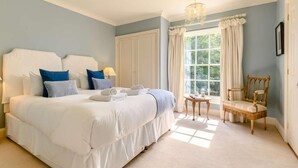 Un dormitorio con una cama grande, una silla, una ventana con cortinas y un candelabro.