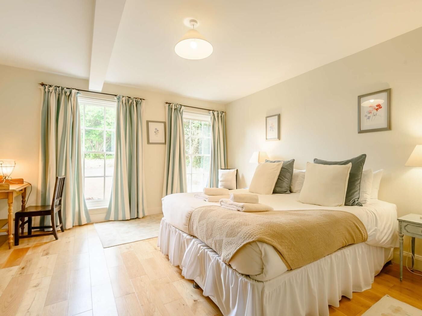A bedroom with a large bed, a desk, and two windows with curtains.