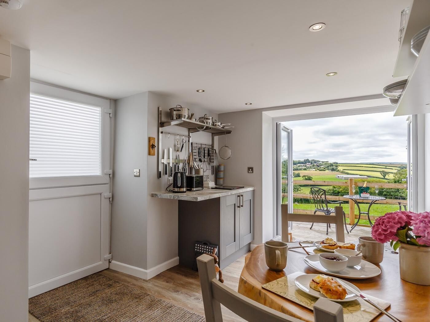 A kitchen with a dining area, a view of the countryside, and a table set for two with food.