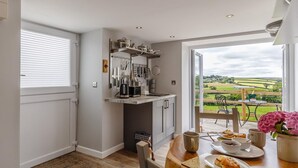 A kitchen with a dining area, a view of the countryside, and a table set for two with food. - 1 Bed in Launceston (oc-78428) (Boyton)