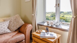 A cozy room with a leather sofa, a small wooden table with a book and teapot, and a window with a view of greenery. - 1 Bed in Launceston (oc-78428) (Boyton)