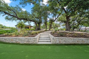 A pathway leading to a building surrounded by mature trees and a well-maintained lawn. - Hill Country Retreat: Walk to Guadalupe River & (Canyon Lake)