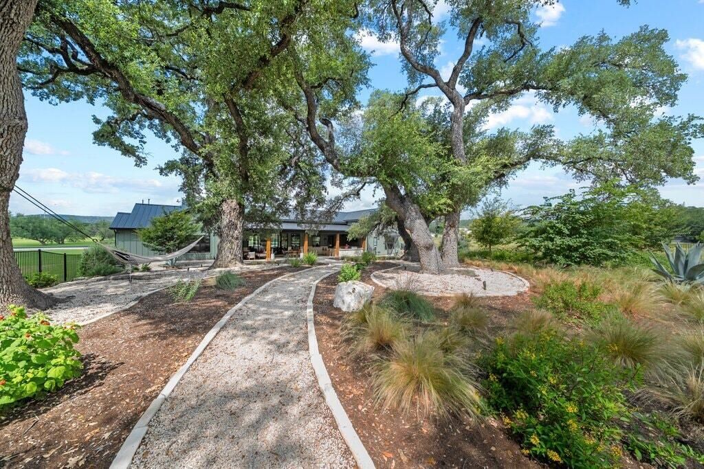 Un jardin aménagé avec un sentier sinueux, de grands arbres et un bâtiment doté d’un toit en pente.