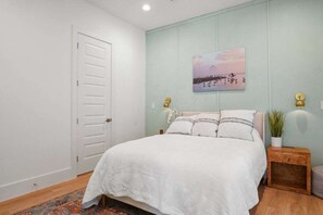 Un dormitorio con una cama, una puerta, un cuadro colgado en la pared y una mesita de noche con una lámpara.