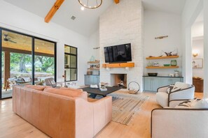 A modern living room with a fireplace, a large TV, and a sofa. - Hill Country Retreat: Walk to Guadalupe River & (Canyon Lake)