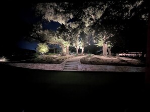 A nighttime outdoor area with a stone pathway leading to a seating area under trees, illuminated by ground lights. - Hill Country Retreat: Walk to Guadalupe River & (Canyon Lake)