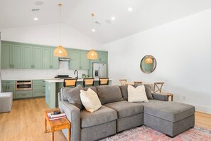 Eine moderne Küche mit grünen Schränken, einem grauen Sofa und Pendelleuchten.