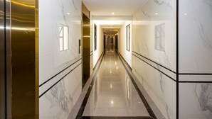 Un largo pasillo estrecho con paredes de mármol y suelo reflectante, que conduce a una puerta al final.