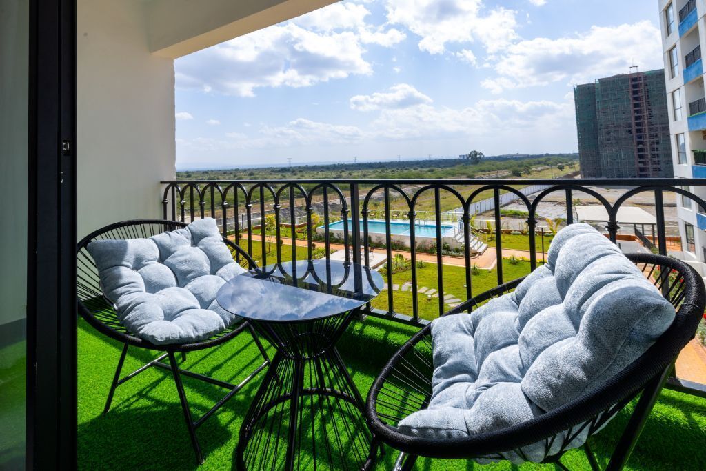 Un balcón con dos sillas y una mesa, vista a una piscina y un edificio al fondo.