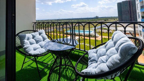 Un balcón con dos sillas y una mesa, vista a una piscina y un edificio al fondo.