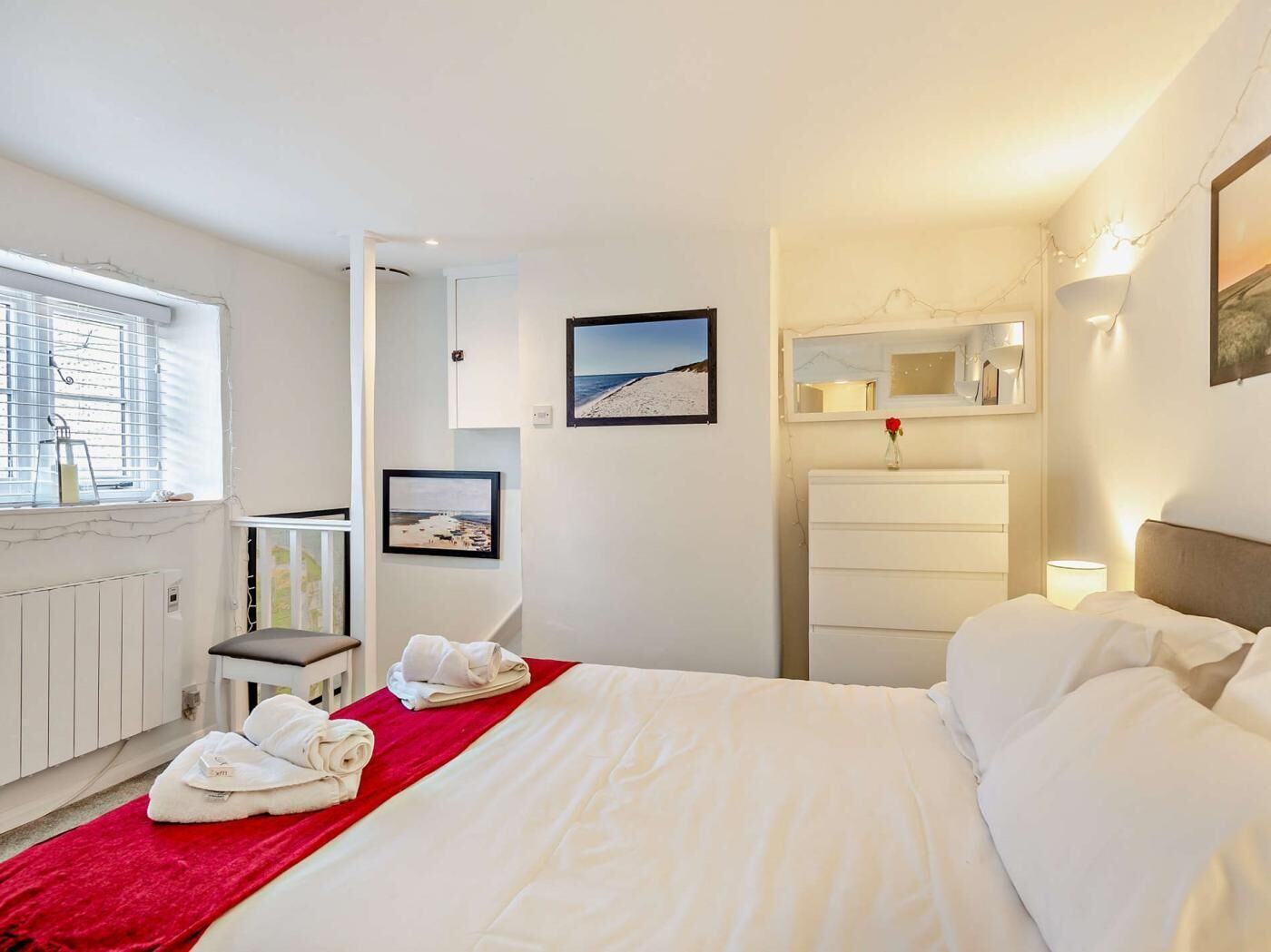 Ein Hotelzimmer mit Bett, Schreibtisch, Stuhl, Heizkörper, Fenster mit Jalousien und einer Wand mit gerahmten Bildern.