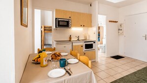 Cocina compacta con microondas, horno y pileta. Se observa una mesa de comedor puesta con platos, un vaso y una botella de jugo de naranja.