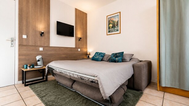 Habitación de hotel moderna con una cama, un televisor de pantalla plana, una mesita con cafetera y un cuadro en la pared.