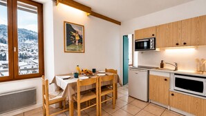 Cocina compacta con comedor, armarios de madera, microondas y vistas a un paisaje nevado.