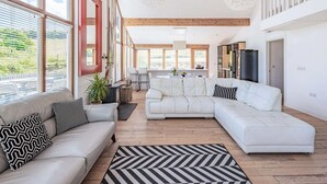 Un amplio espacio de sala con un ventanal grande, un sofá blanco, un tapete blanco y negro, y un comedor con mesa y sillas.