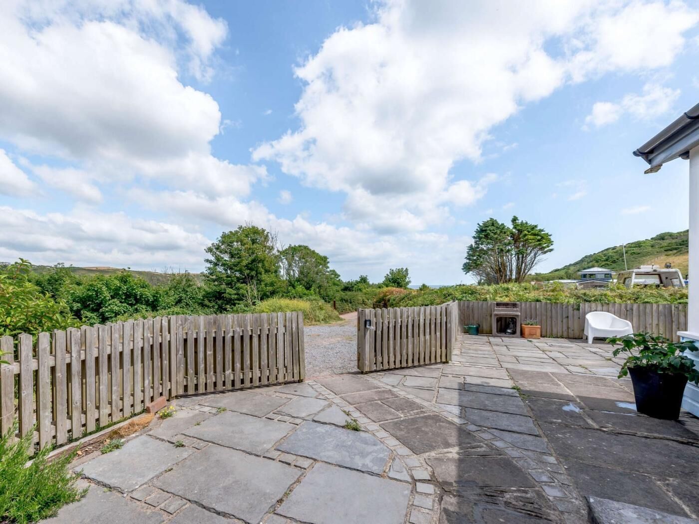A stone patio with a wooden fence, a barbecue area, and a white chair.