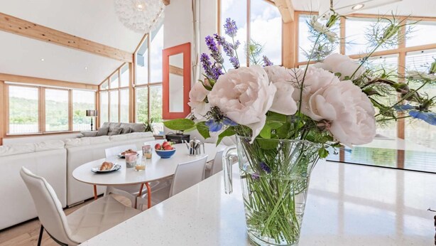 Una cocina moderna con comedor, ventanas amplias y un jarrón de flores en la encimera.