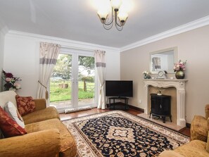 A living room with a fireplace, television, and a large window with curtains. - 4 Bed in Penrith (oc-80541) (Ousby)