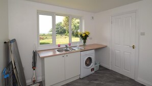 Een wasserette met een wasmachine, een wastafel en een raam met uitzicht op het buitenland.