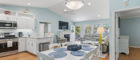 A modern kitchen with white cabinets, a dining area with a table and chairs, and a living room with a sofa and a lamp.