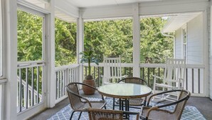 Een overdekte veranda met een tafel, stoelen, witte leuningen en een plafondventilator.