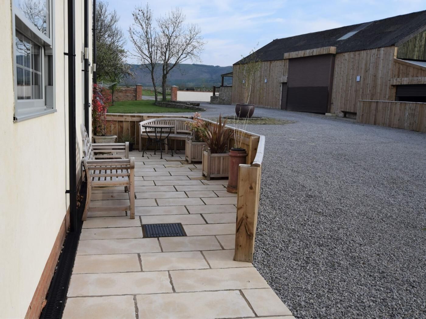 Une terrasse avec des meubles d’extérieur, une allée en gravier et un bâtiment en bois en arrière-plan.