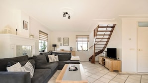 Ein Wohnzimmer mit einem dunkelgrauen Sofa, einem Holztisch, einem Fernsehschrank und einer Treppe.