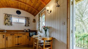 Een houten interieur met een keuken, een eettafel, stoelen en een raam met gordijnen.