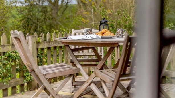 Een houten tafel met stoelen, een lantaarn en een bord eten.