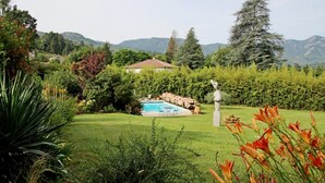 A residential property with a swimming pool, lush greenery, and a mountainous backdrop.