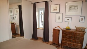 A bedroom with a bed, a dresser, a mirror, and a window with curtains. - Guest Room in Family Home – The Engraving Room at the Foot of the Monts d'Ardèche (Jaujac)