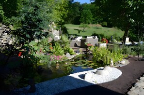 A garden with a pond, seating area, and a grassy field in the background.